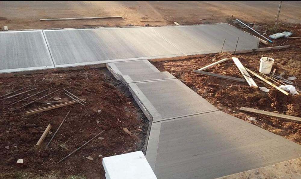 Newly poured concrete sidewalk with ramp and road, in dirt lot.