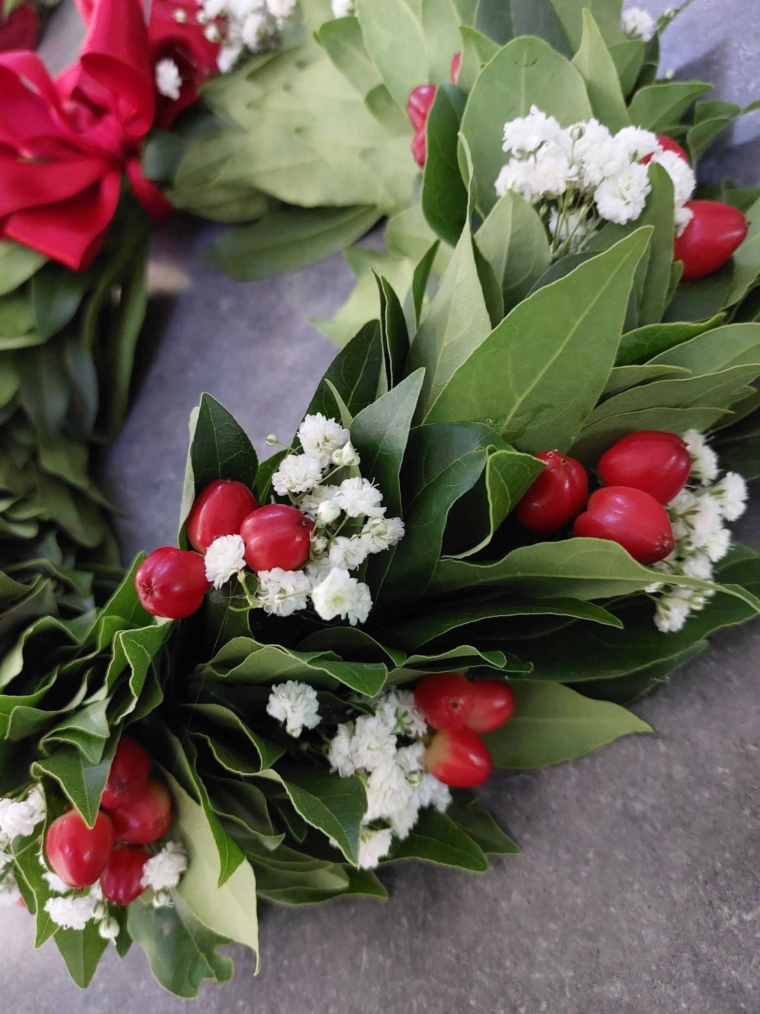 Ghirlanda composta da foglie verdi, bacche rosse e fiori bianchi, con un fiocco rosso.