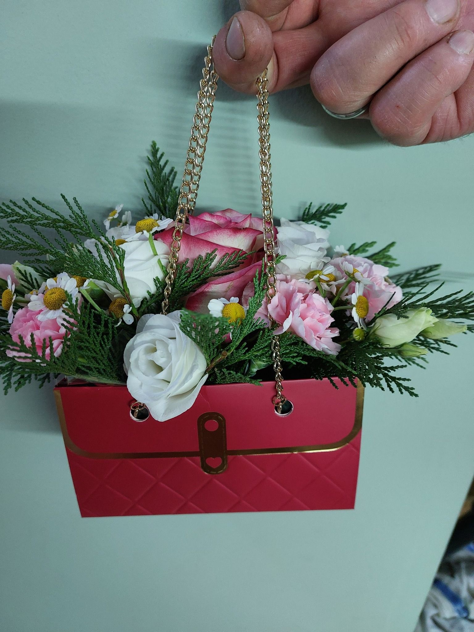 Composizione floreale a forma di borsetta rossa con fiori rosa e bianchi, tenuta in mano.
