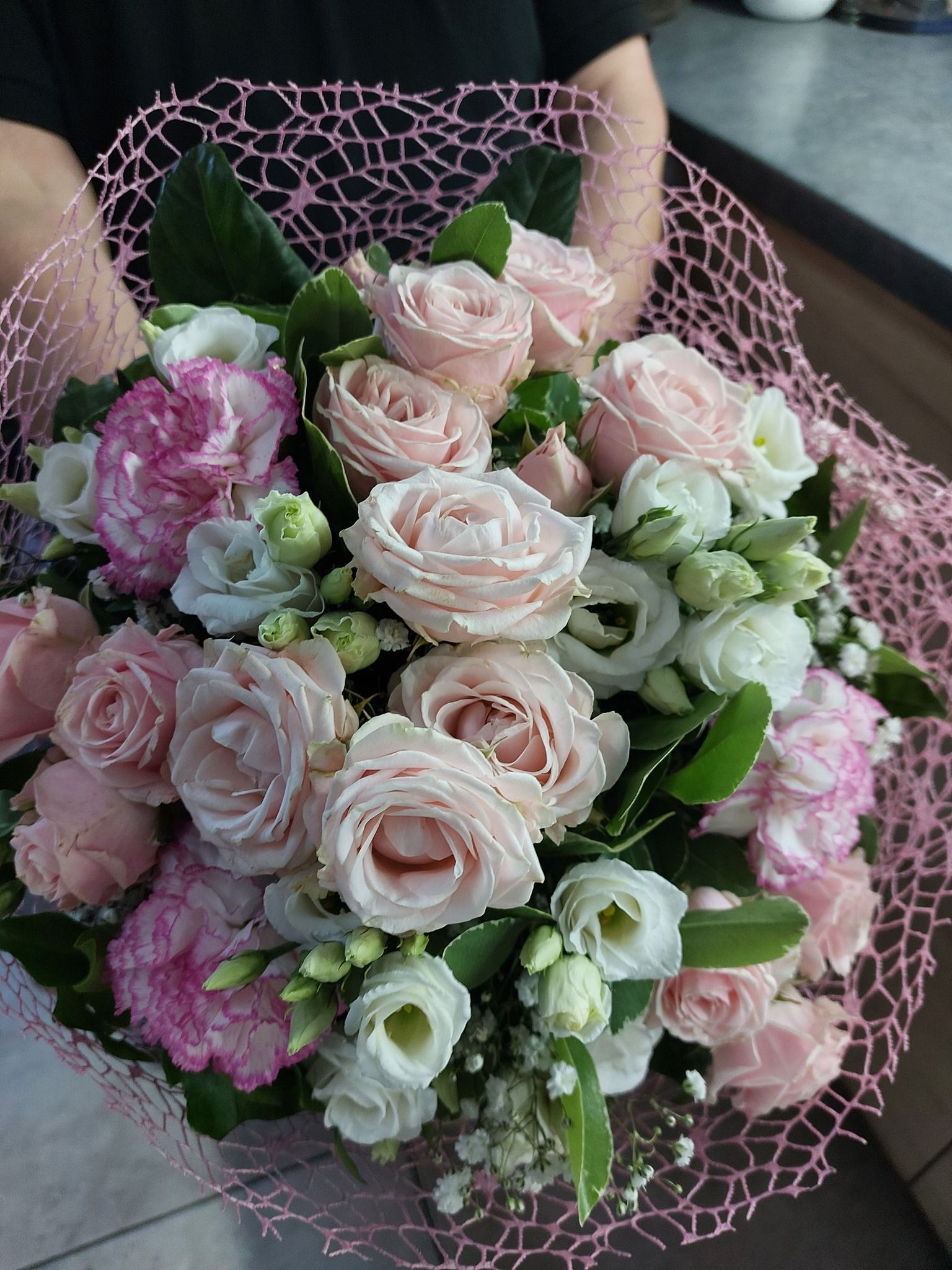 Composizione floreale con rose rosa, gigli bianchi e foglie verdi.