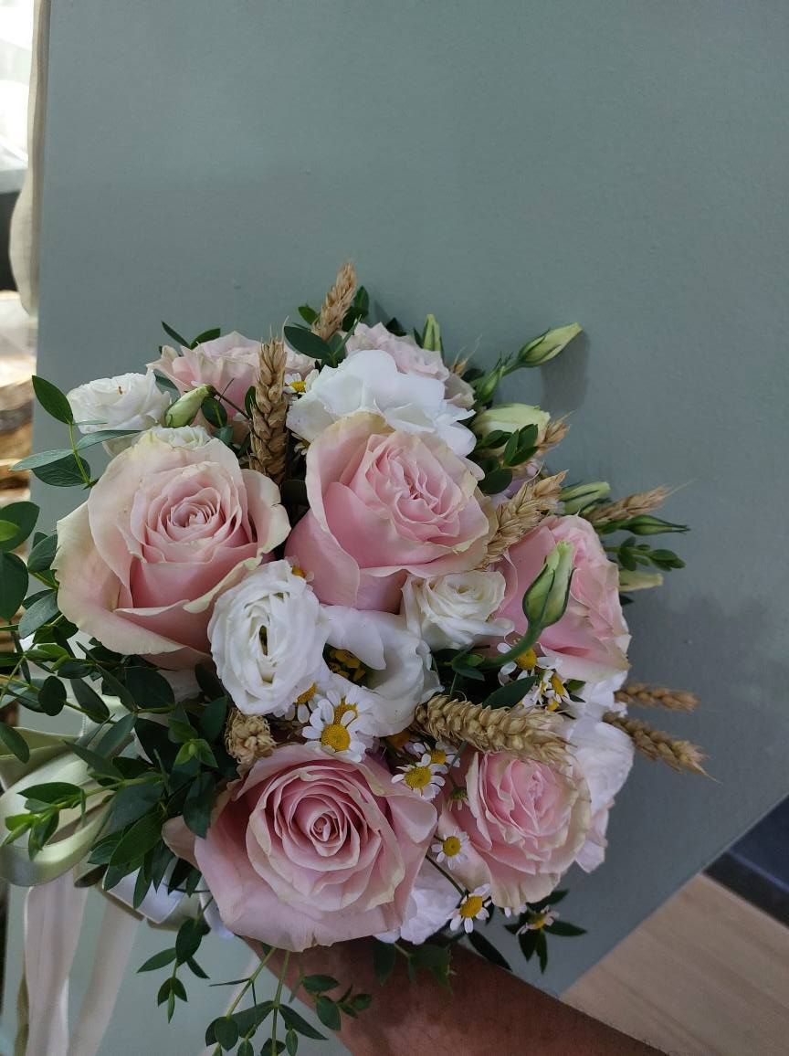 Bouquet di rose rosa, fiori bianchi e grano, con fogliame verde su un muro grigio-verde.