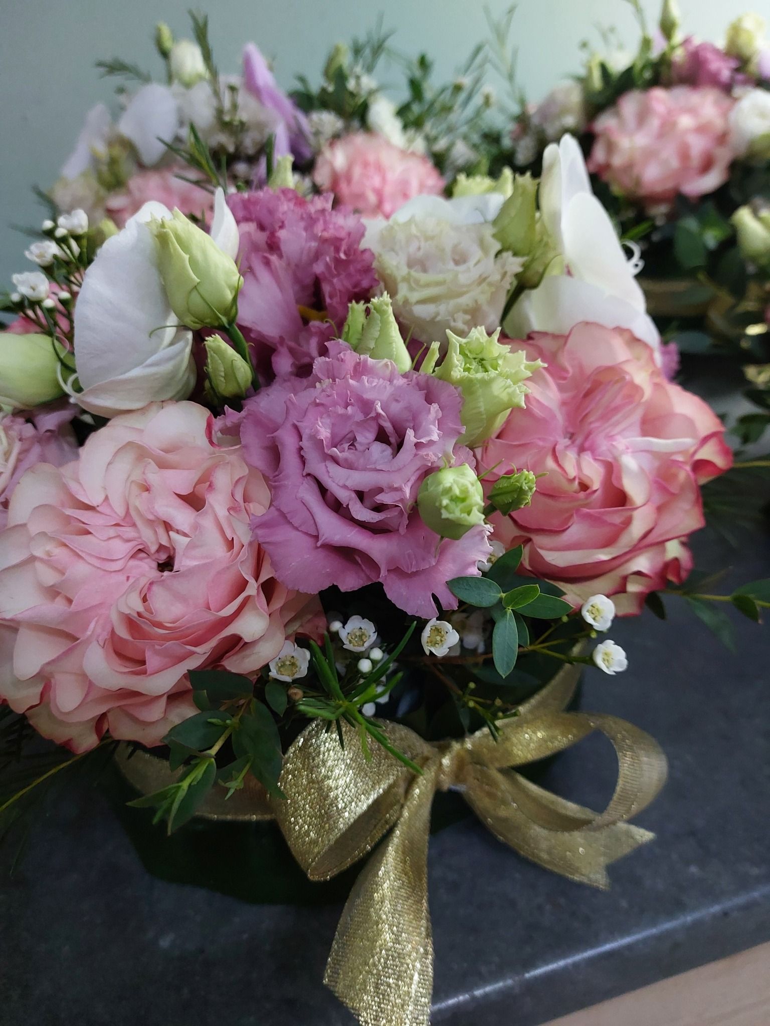 Primo piano di una composizione floreale con fiori rosa, viola e bianchi e un nastro dorato.