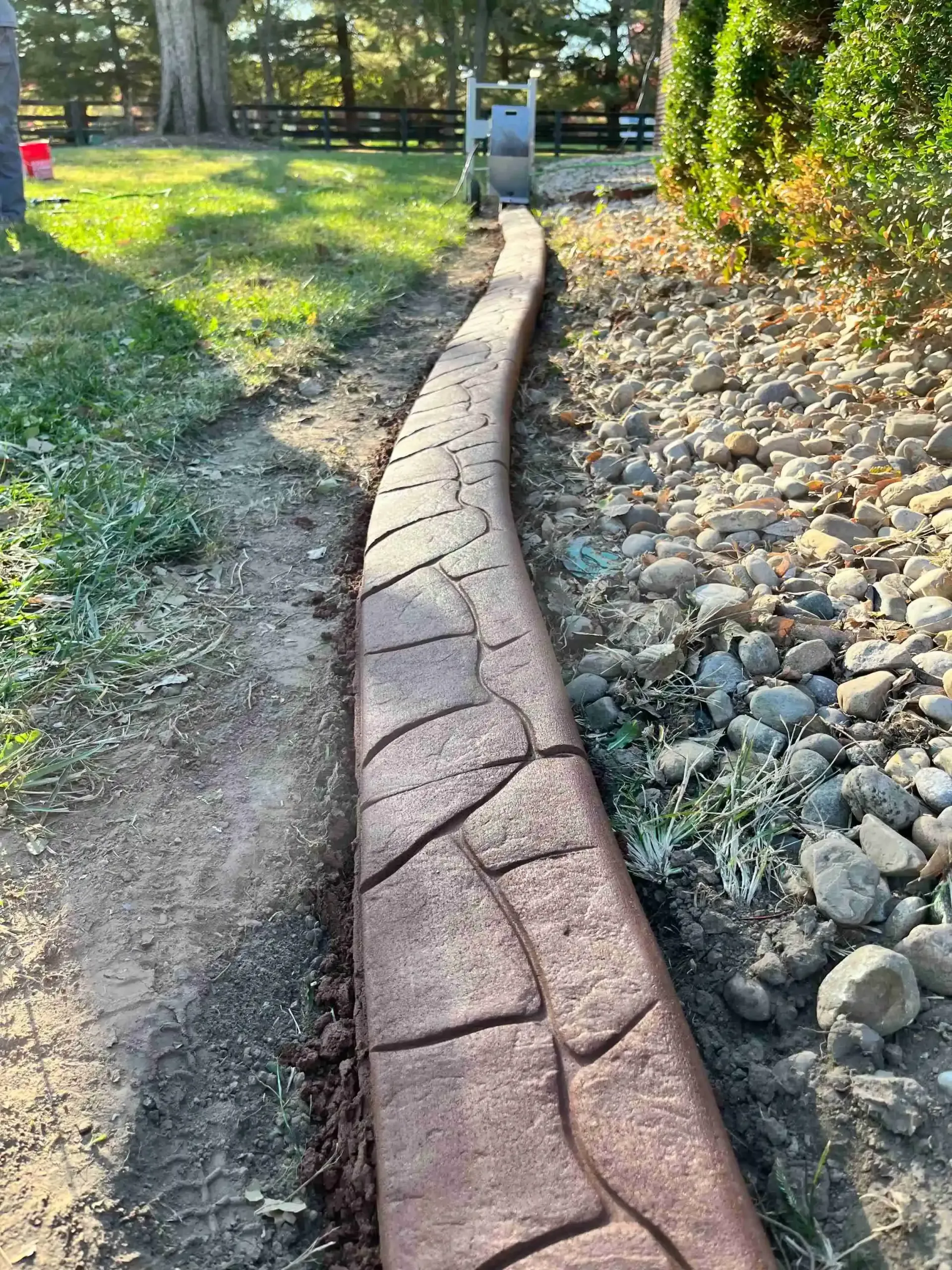 A concrete curb is sitting next to a rocky path in a yard.
