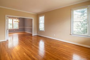 Empty room with hardwood floors, beige walls, white trim, and three windows.