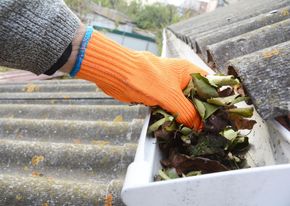 Person wearing orange glove cleaning leaves from a gutter on a roof.
