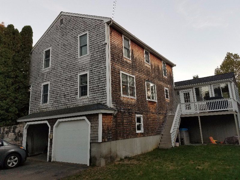 Three-story shingled house with garage, porch, and exterior staircase beside a grassy yard