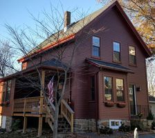 Two-story brown house with a small front porch and steps, set in a leafless yard at dusk