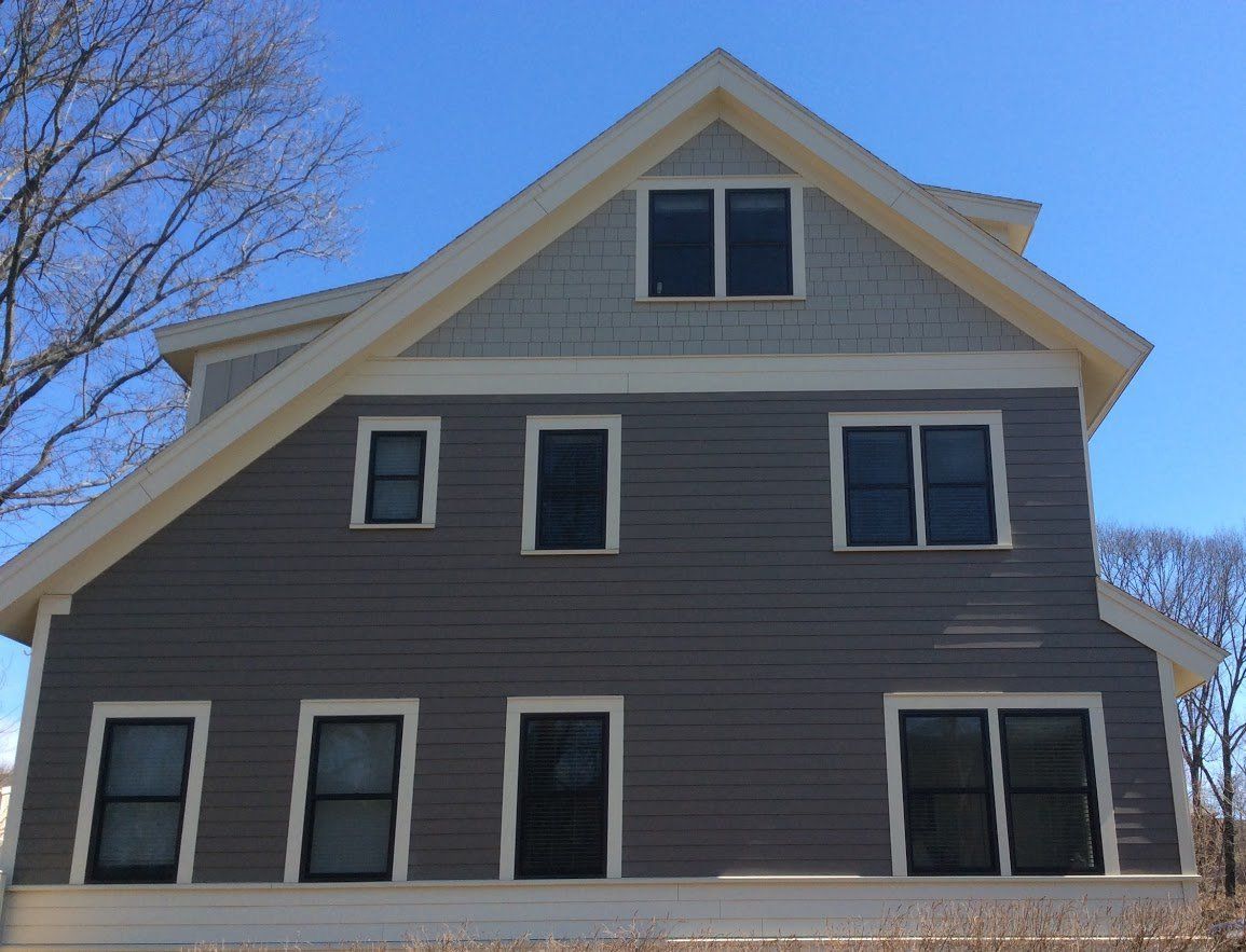 Gray and light-blue house exterior with black-framed windows against a blue sky. Windows & Doors | MasterCraft Roofing, Siding & Windows | Serving Eastern MA, NH & Selected Areas of VT