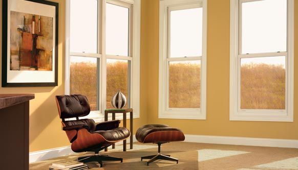 Modern living room with leather lounge chair, ottoman, framed art, and large windows letting in warm light