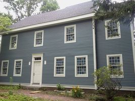 Blue-gray two-story house with white trim and multiple windows, viewed from the front yard
