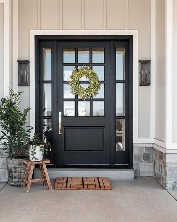 Black front door with glass panes, wreath, and matching side lights, flanked by sconces. Windows & Doors | MasterCraft Roofing, Siding & Windows | Serving Eastern MA, NH & Selected Areas of VT