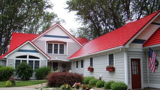 White house with red roof and flower boxes, surrounded by trees and shrubs, with an American flag by the entry.