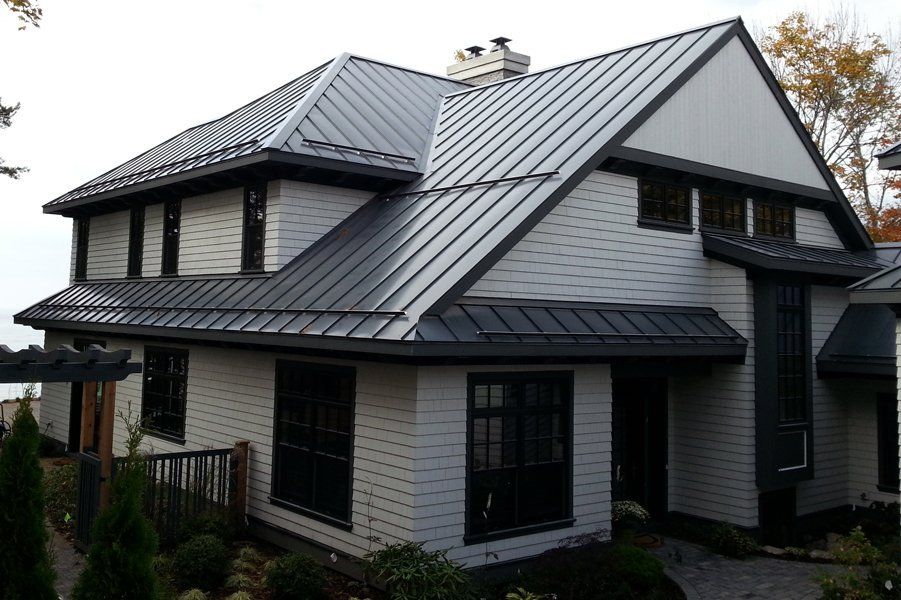 Gray house with dark gray metal roof and black window frames. Roofing | MasterCraft Roofing, Siding & Windows | Serving Eastern MA, NH & Selected Areas of VT
