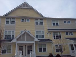 Three-story beige apartment building with white trim and gabled roof entrance