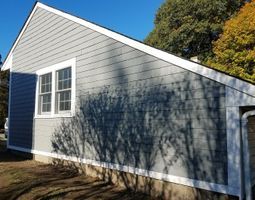 White-sided house exterior with a gabled roof, windows, and tree shadows on the wall