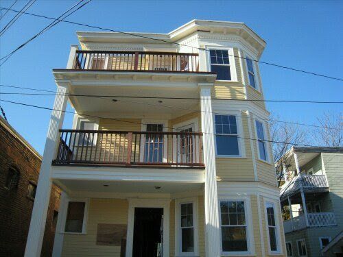 Three-story beige house with balconies and a blue sky above