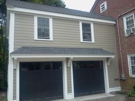 Two-car garage with beige siding and dark doors beneath a small upper window.