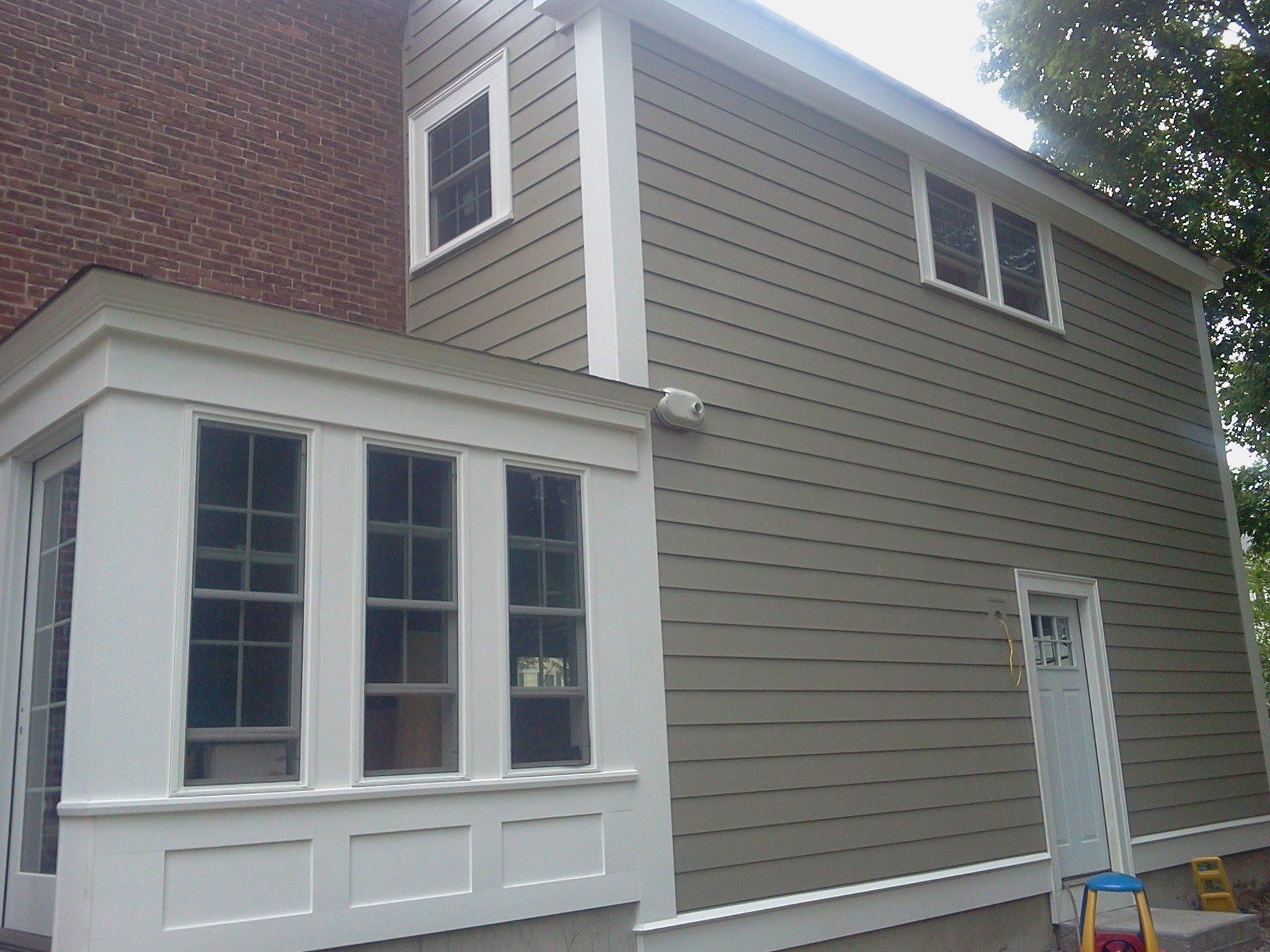 Two-story tan house with white trim and a small front porch under a cloudy sky