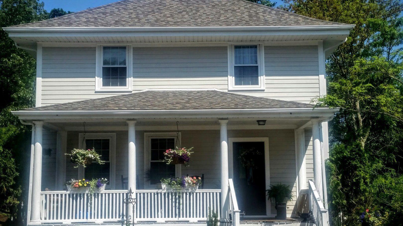 Two-story beige house with a white porch, hanging flower baskets, and a dark front door