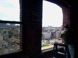 Person stands by a window in a brick building, overlooking a cityscape.