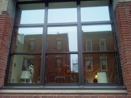 Brick building window reflecting nearby buildings and a lit lamp inside