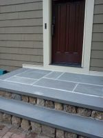 Front porch with gray steps and stone trim leading to a dark brown front door.