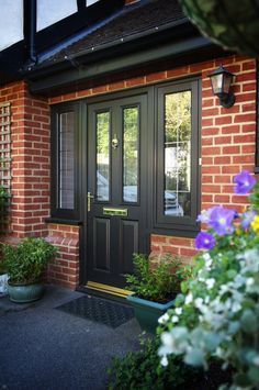 Front entrance of a brick house with a black door, windowed sidelights, and potted flowers