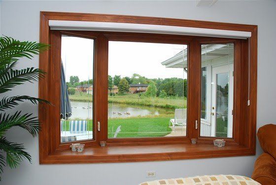 Wood-framed picture window overlooking a green backyard and patio, with indoor plants and a couch edge visible