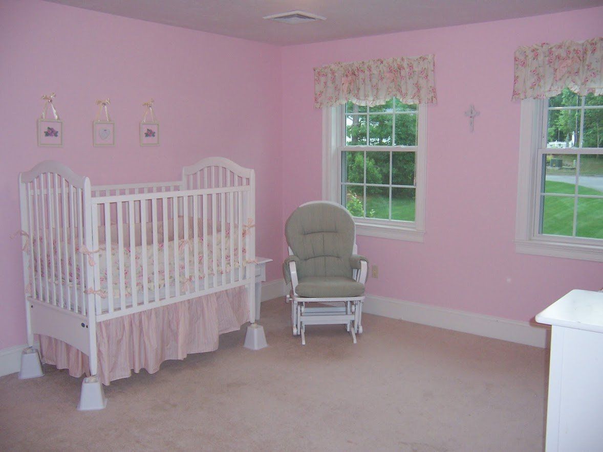 Pink nursery with white crib, rocking chair, and two windows