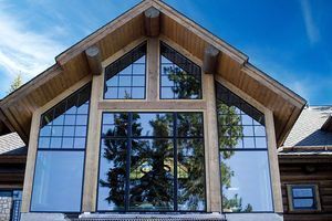 Large A-frame house facade with tall windows and wood trim under a blue sky