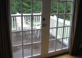Sliding glass doors to a wooden deck with white chairs and railing, viewed from inside a room