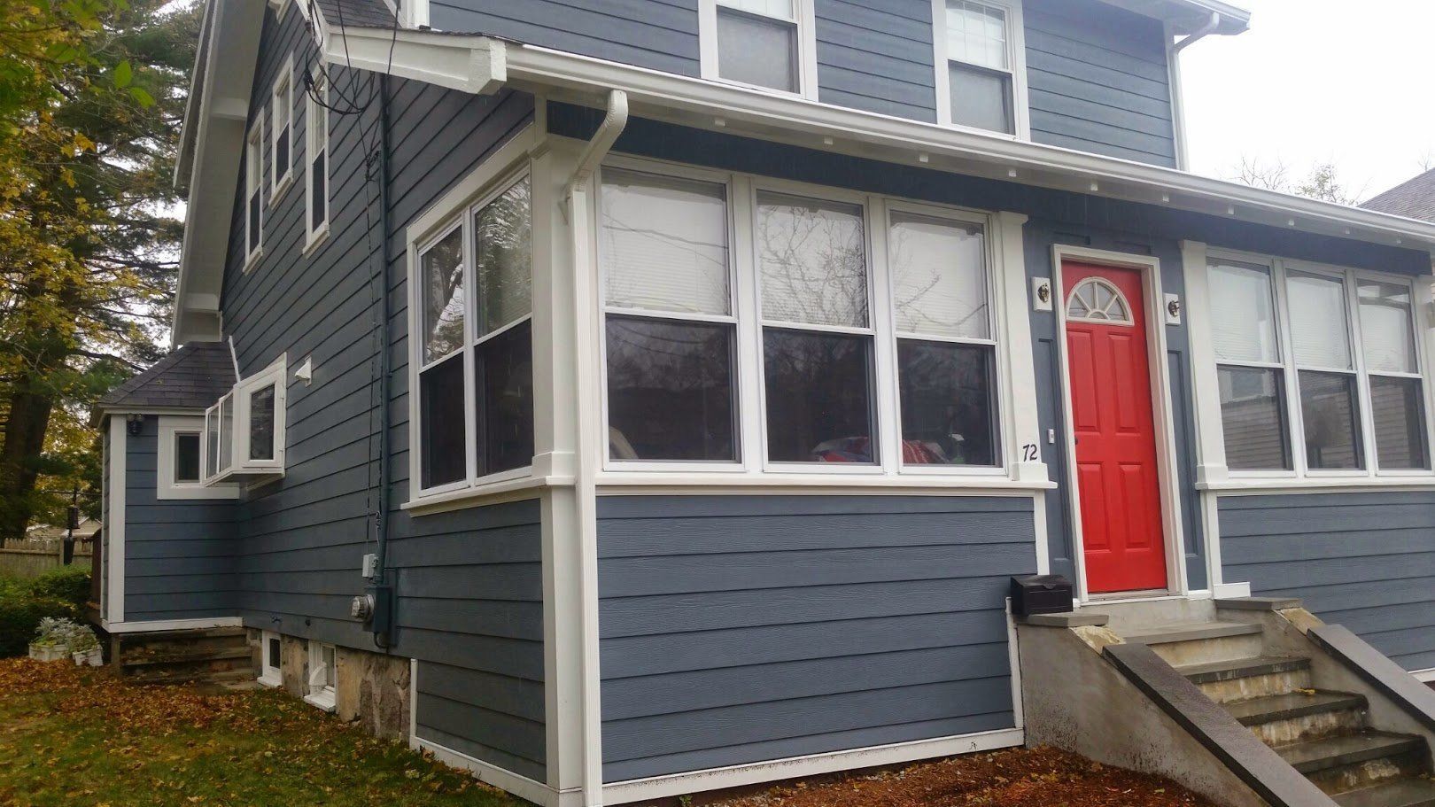 Blue-gray house exterior with white trim, a bright red front door, and front steps under an overcast sky