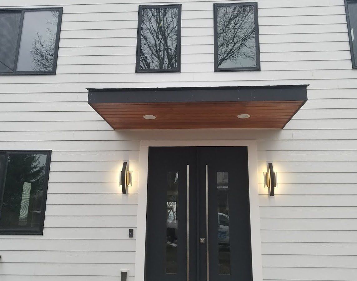 Modern white house exterior with black double doors and a wood awning over the entrance