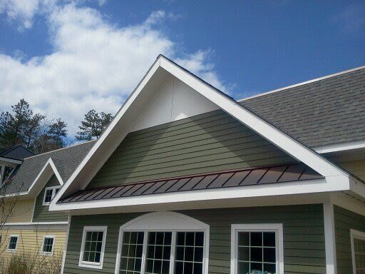 Green and beige house exterior with white trim and a gabled roof under a blue sky