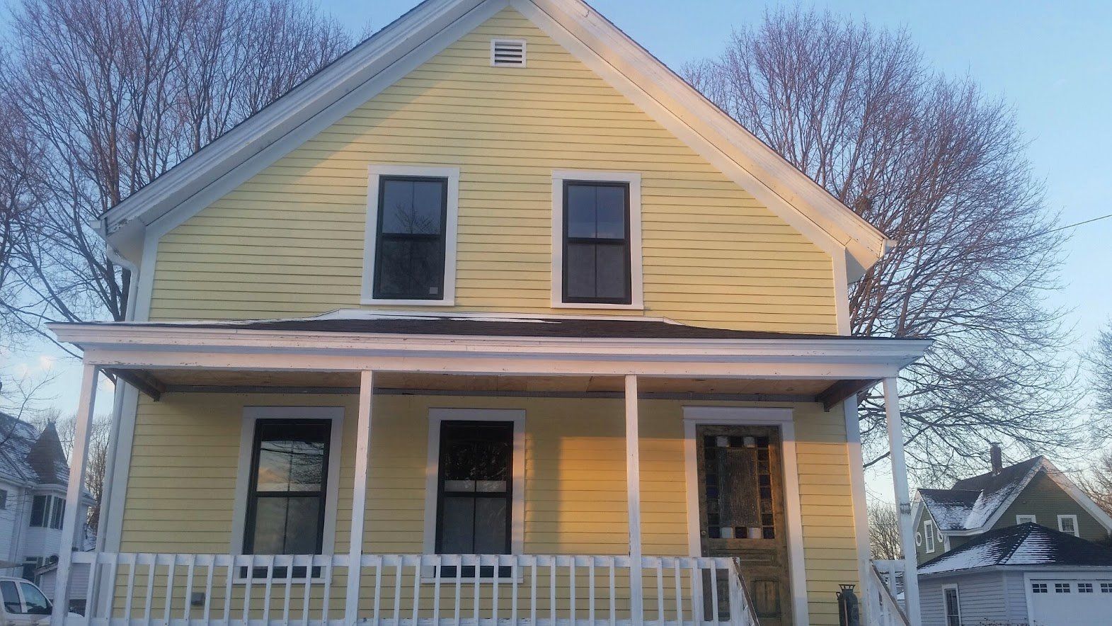 Yellow two-story house with a front porch and white railing in a snowy yard