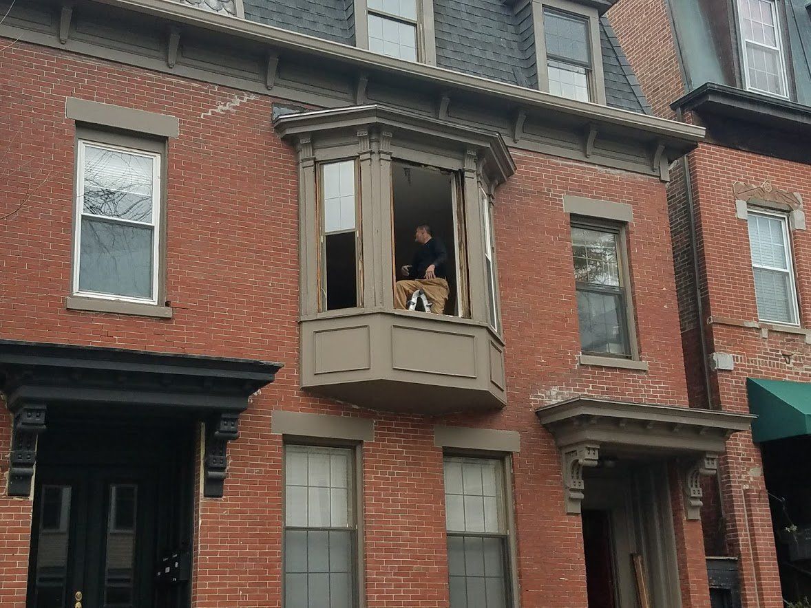 Red brick row house with a person standing in an open second-floor bay window.