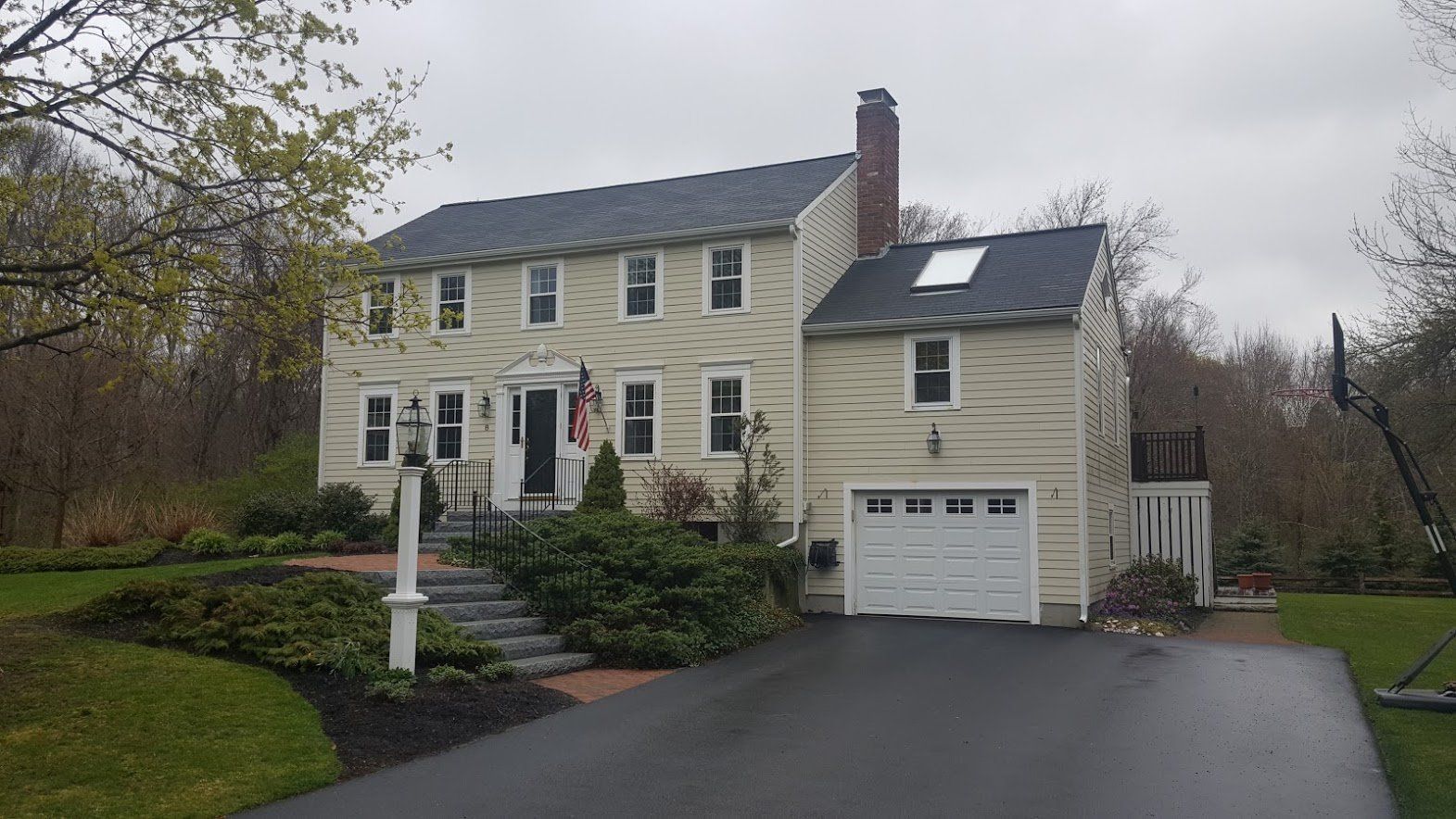 Two-story beige house with garage, dark roof, front lawn, and driveway on a cloudy day