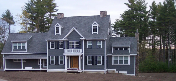 Large gray two-story house with white trim and a porch, set among trees at dusk