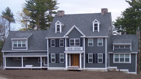 Gray two-story house with white trim, dormer windows, and a covered porch, surrounded by trees.