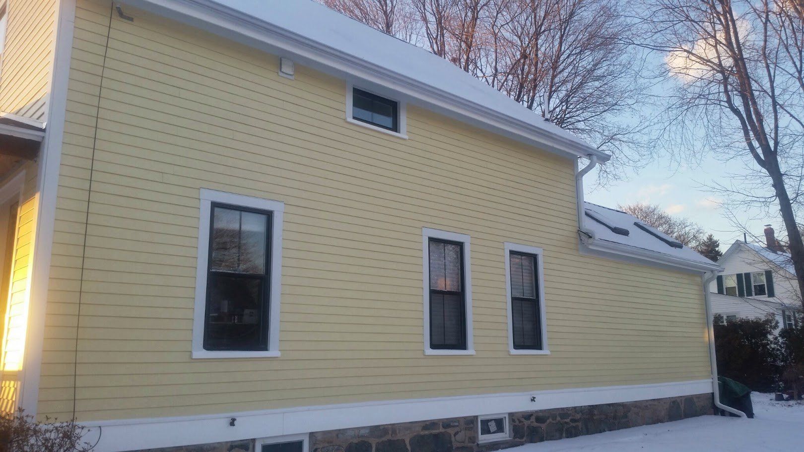 Yellow house exterior with three windows and snow on the roof in winter.