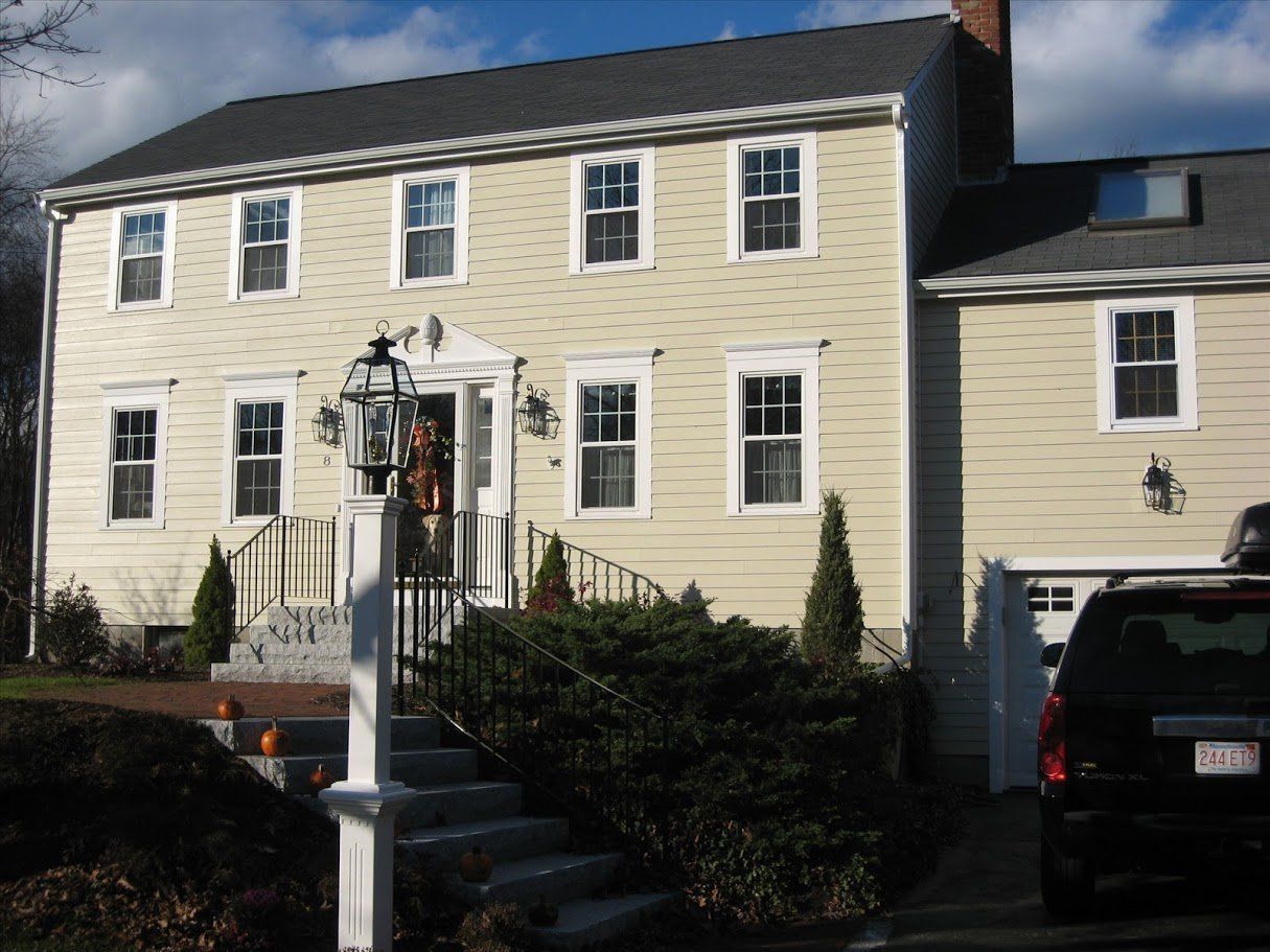 Two-story beige house with white trim, front steps, shrubs, and a parked black SUV in the driveway