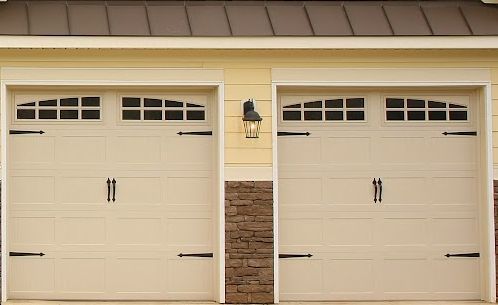 Two beige garage doors with black decorative hardware and arched windows. MasterCraft Roofing, Siding & Windows | Serving Eastern MA, NH & Selected Areas of VT