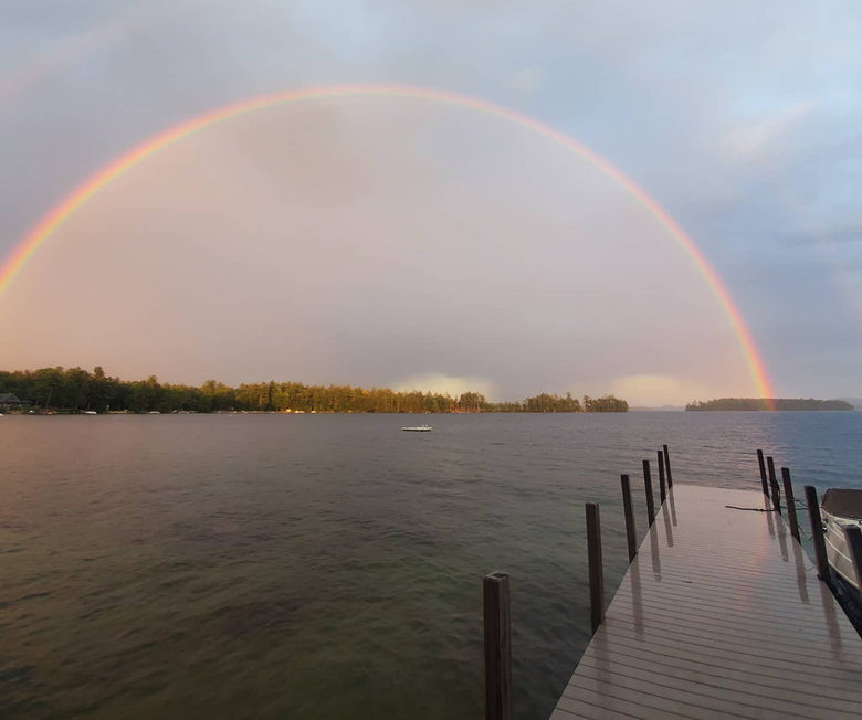 Rainbow over a calm lake at sunset, with a wooden dock extending into the water