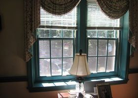 Window with teal trim, scalloped curtains, and a table lamp on the sill in a dim room