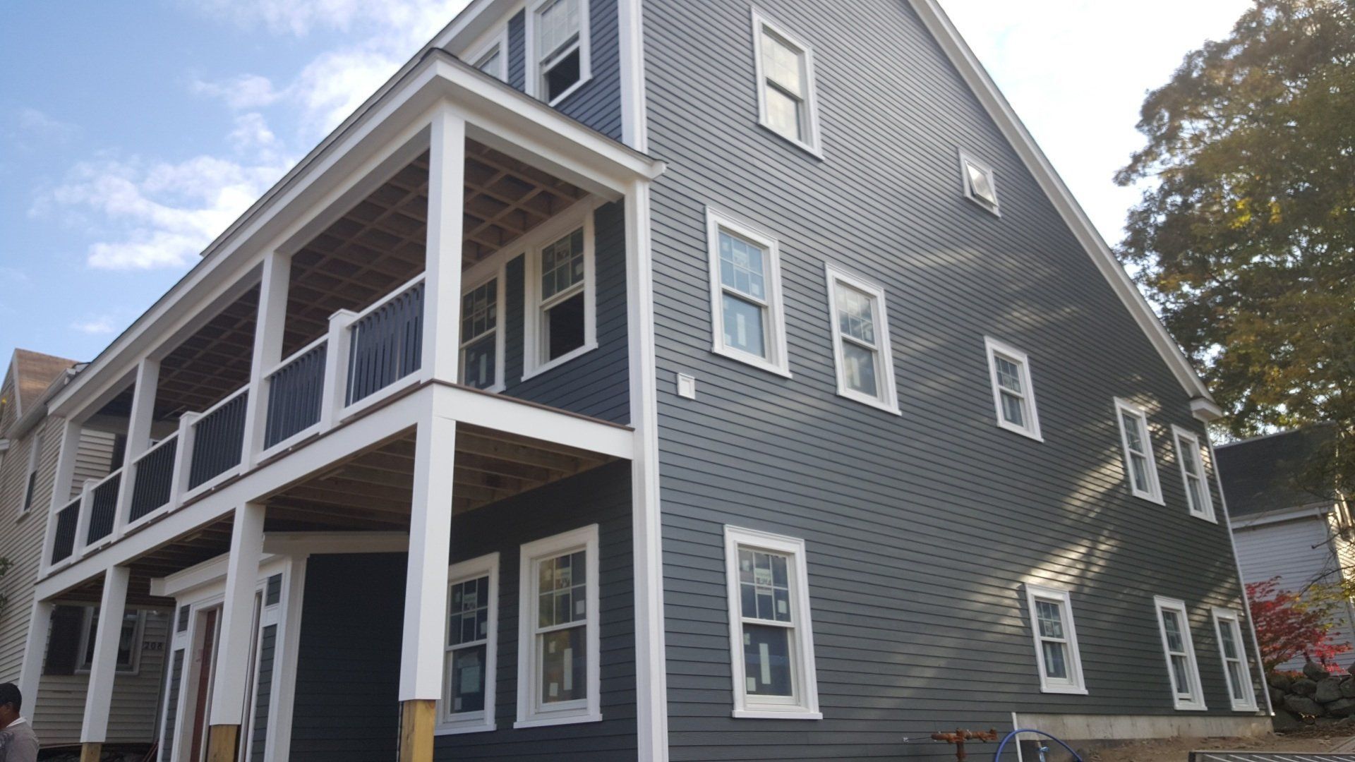 Gray two-story house with white trim and wraparound porch under a blue sky