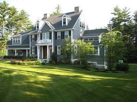 Large gray house with white trim and a front porch, surrounded by a green lawn and trees