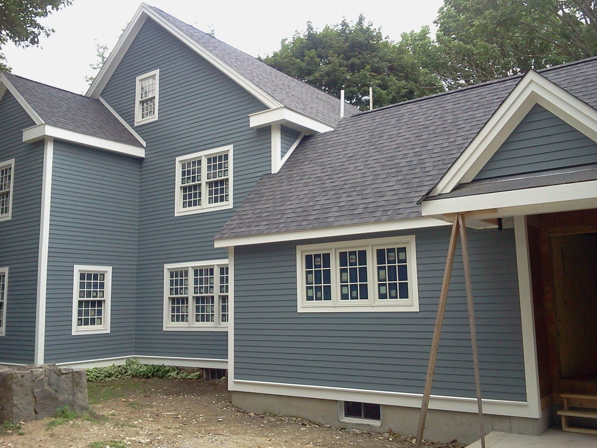Blue-gray house with white trim and gabled roof, shown from the side in a wooded yard