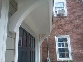 Brick building entrance with arched white canopy, dark double doors, and nearby windows with window air conditioner