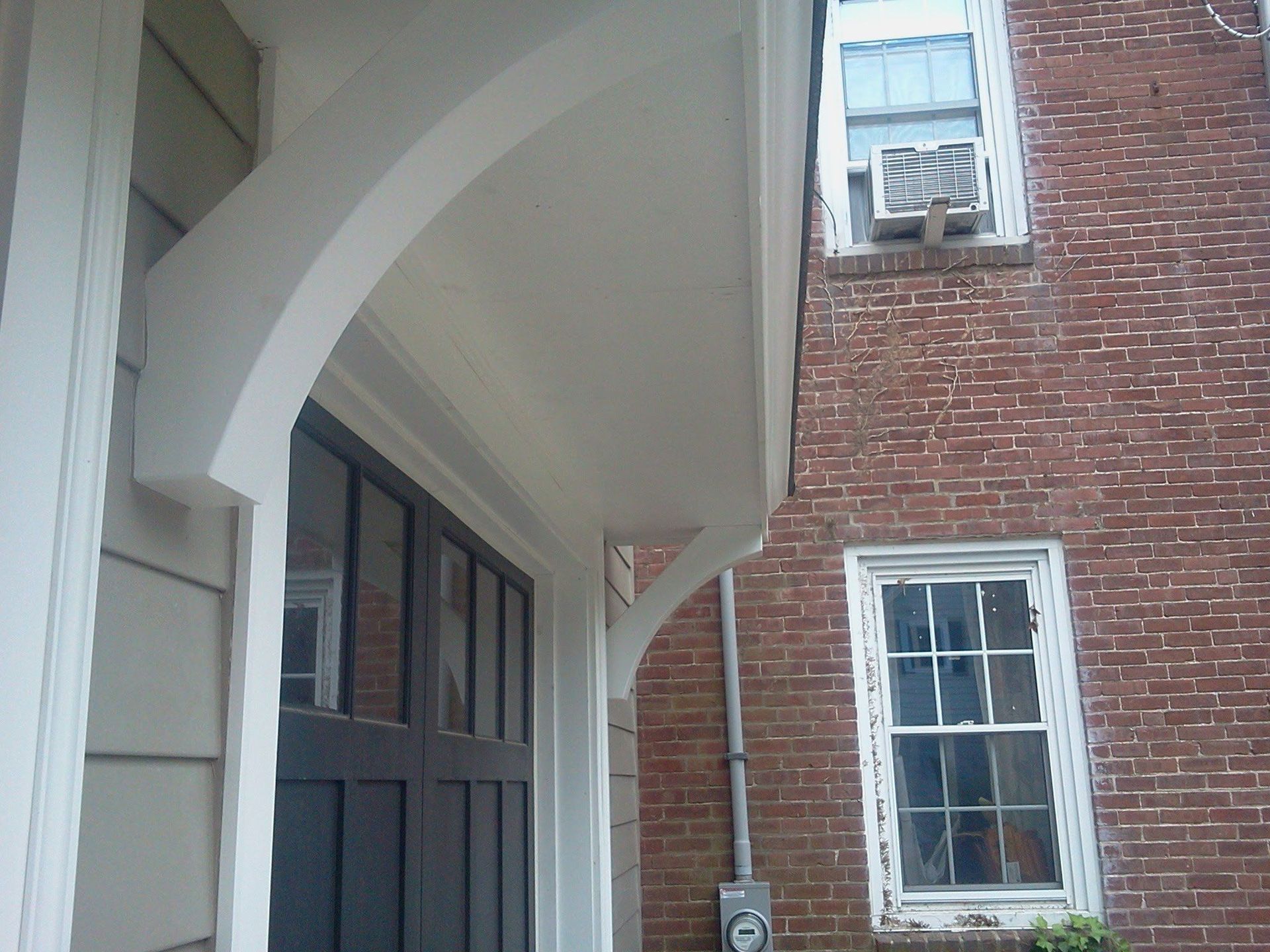 Brick building exterior with white arched awning and windows beside a gray doorway