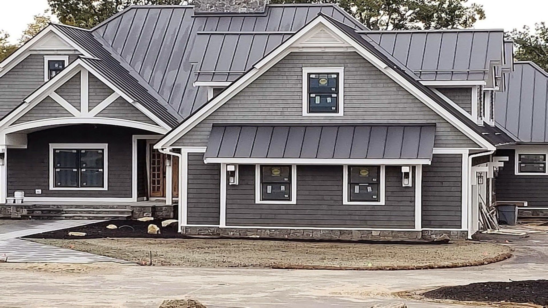 Gray two-story house under construction with gabled roof, front porch, and unfinished landscaping